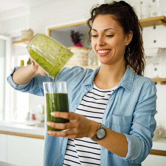 Grüne Smoothies zum Start in den Tag - auf den Inhalt kommt es an. Frau bereitet sich einen grünen Smoothie vor.