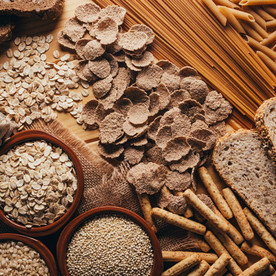 Vollkornprodukte Eine Auswahl an Vollkornprodukten wie Vollkornbrot, -nudeln, -reis und verschiedenen Getreidesorten auf einem Holztisch, zur Veranschaulichung einer nährstoffreichen, ausgewogenen Ernährung.